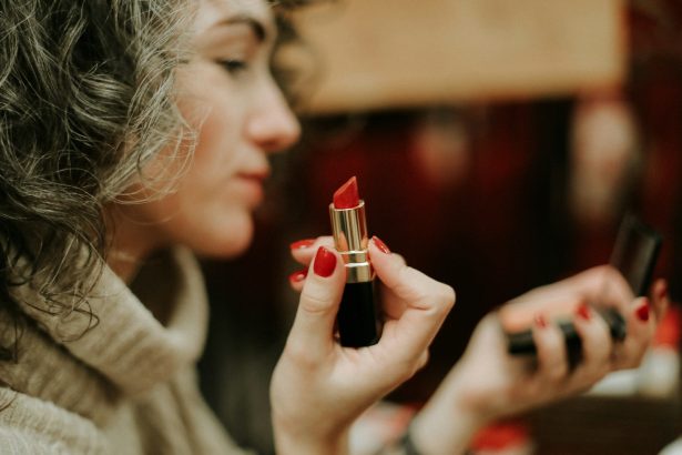 woman in gray sweater holding lipstick