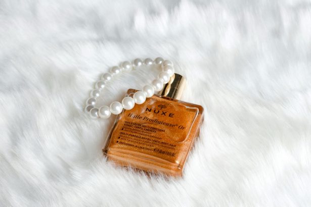 From above golden face oil in refined bottle placed with pearl bracelet on white cozy plaid